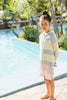 Young girl in a striped dress standing by a pool with greenery in the background